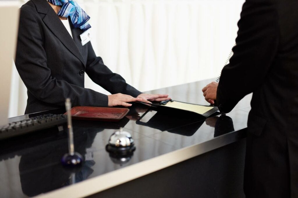 Una receptionist in divisa porge un documento a un ospite al banco dell'hotel, accanto al campanello