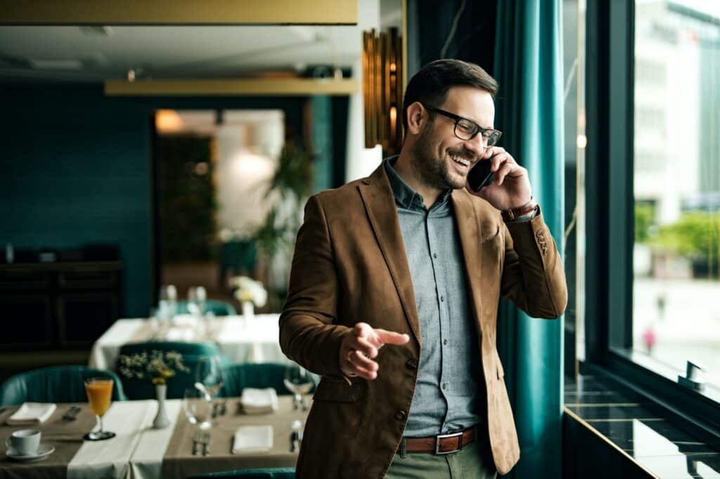 Un uomo sorridente con gli occhiali parla al telefono nella sala di un ristorante