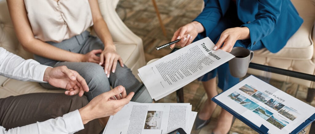 Mani che si passano un modulo di assicurazione di viaggio e un catalogo di destinazioni durante una consulenza