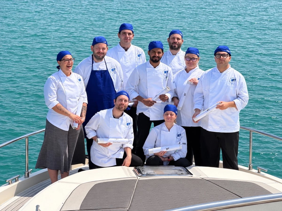 I diplomati chef di IET in giacca bianca e bandana blu sulla prua di uno yacht, con i diplomi in mano